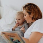 A mother and daughter share a cozy reading moment on a bed, fostering closeness and learning.