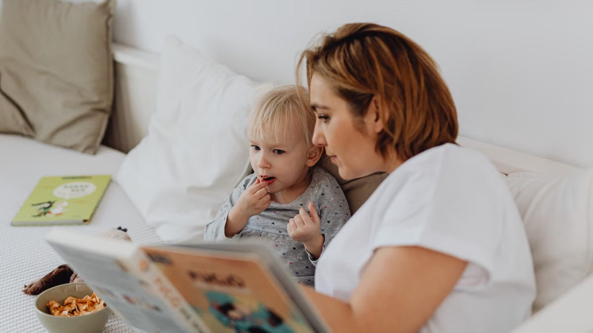 A mother and daughter share a cozy reading moment on a bed, fostering closeness and learning.